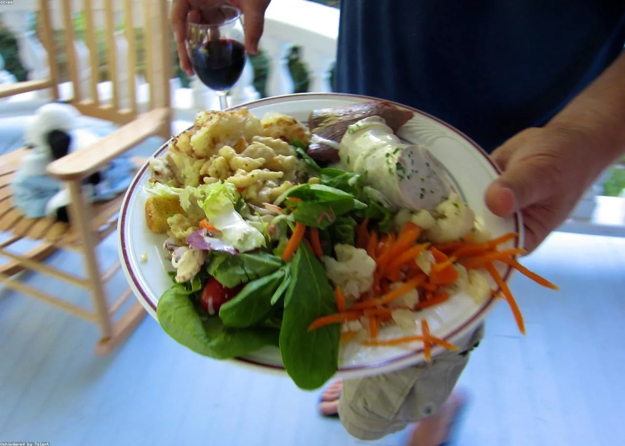 Prato colorido sendo servido com salada, legumes e diferentes preparações